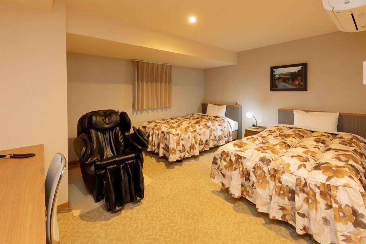 A hotel room with two beds, a leather chair, a desk, and a nightstand.