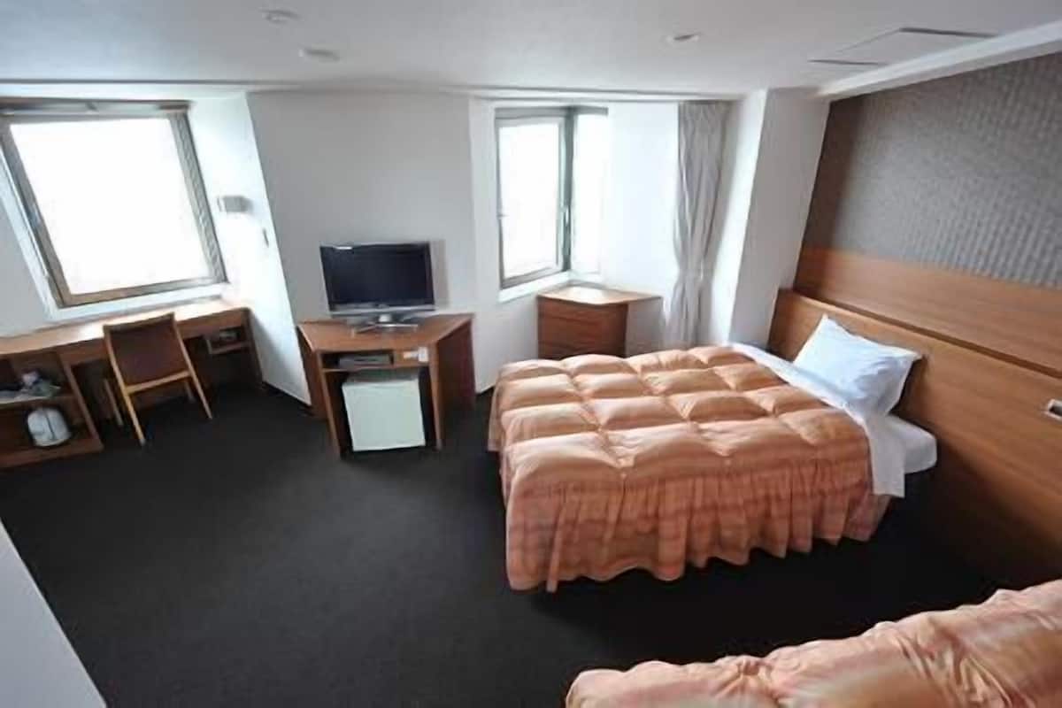 Habitació d'hotel amb llit, escriptori, televisió i finestra.