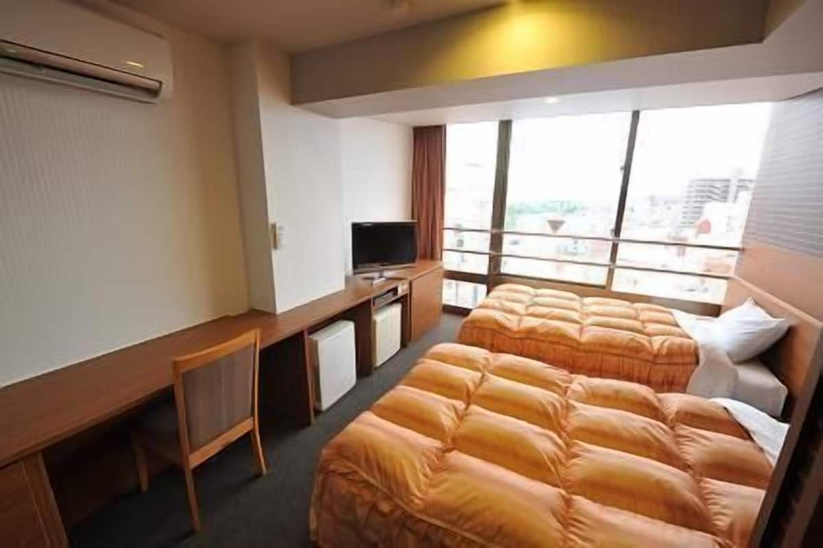 Habitació d'hotel amb dos llits, un escriptori, una televisió i grans finestres.