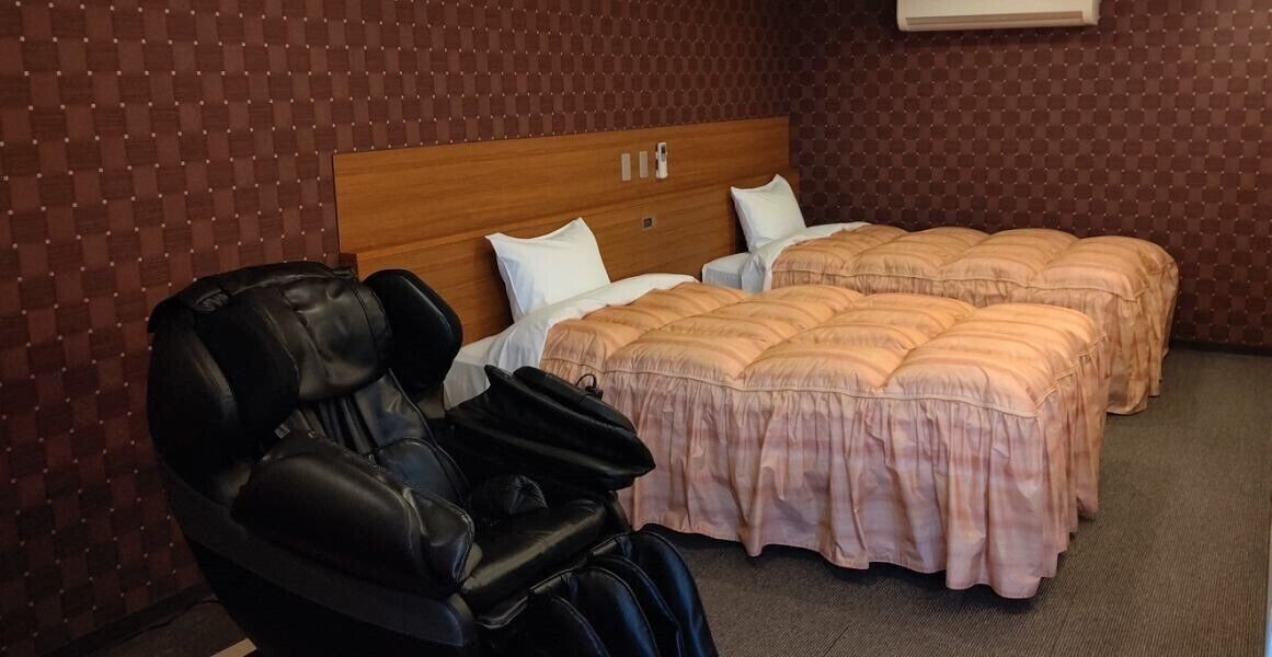 A hotel room with a massage chair, two beds with pink bedding, and a wooden headboard.
