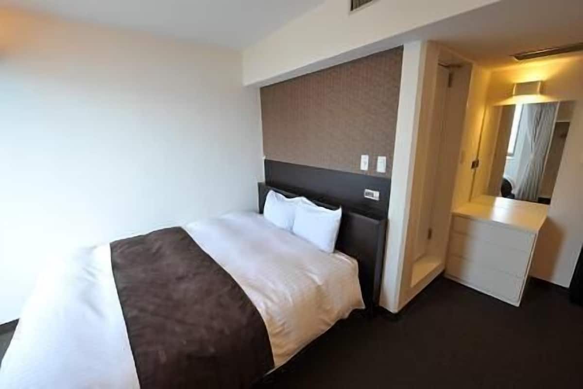 Habitació d'hotel amb un llit, una taula de nit, un mirall i una porta que condueix a una altra habitació.
