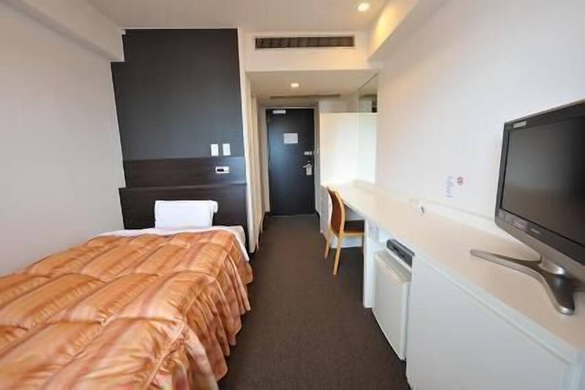 Habitació d'hotel amb un llit, una escriptori, una televisió i una cuineta petita.