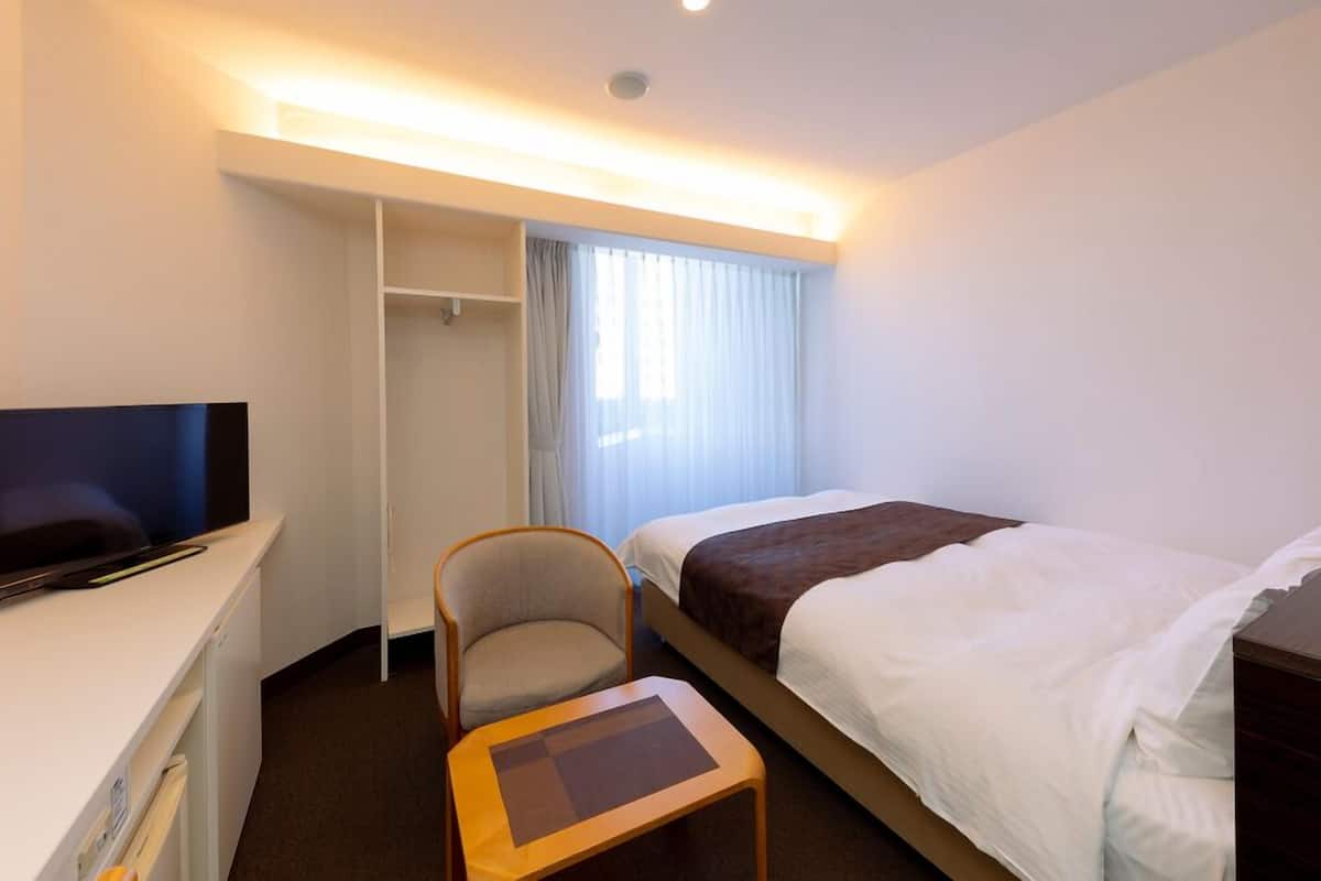 Habitació d'hotel amb llit, televisió, cadira, escriptori i armari.