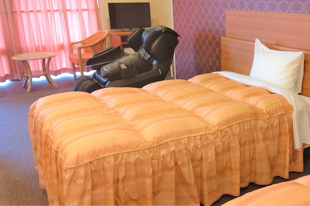 Habitació d'hotel amb llit, cadira de massatge, taula petita i televisió.