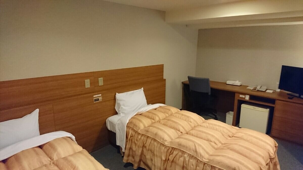 A hotel room with two beds, a desk, a chair, a television, and a small refrigerator.