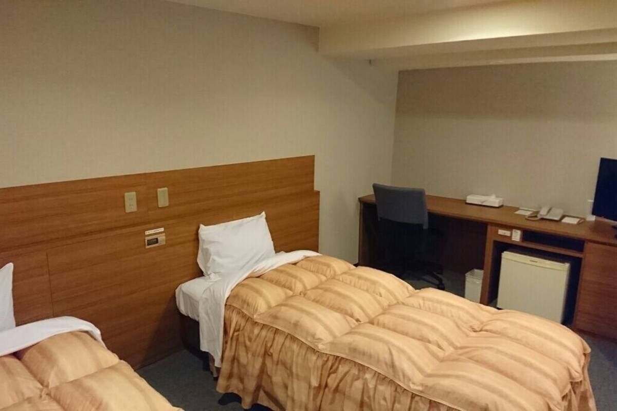 Habitació d'hotel amb dos llits, una taula de treball, una cadira, una televisió i un refrigerador petit.