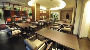 A modern restaurant with multiple tables and chairs, a central light fixture, and a view of the outdoors. - Marugame Plaza Hotel (Marugame)