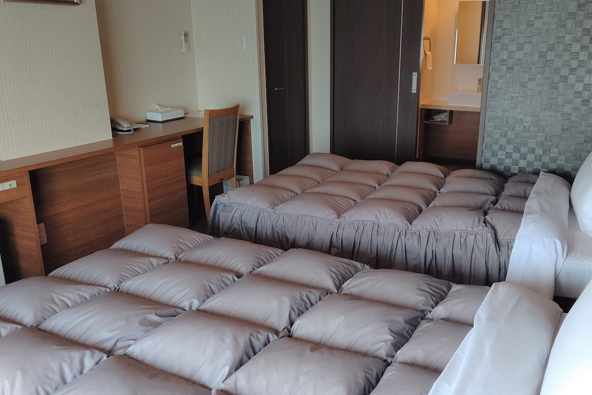 Habitació d'hotel senzilla amb dos llits, un taulell petit i un bany visible per una porta.