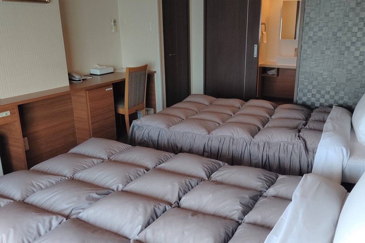Een kleine hotelkamer met twee bedden, een bureau en een zichtbare badkamer door een deur.