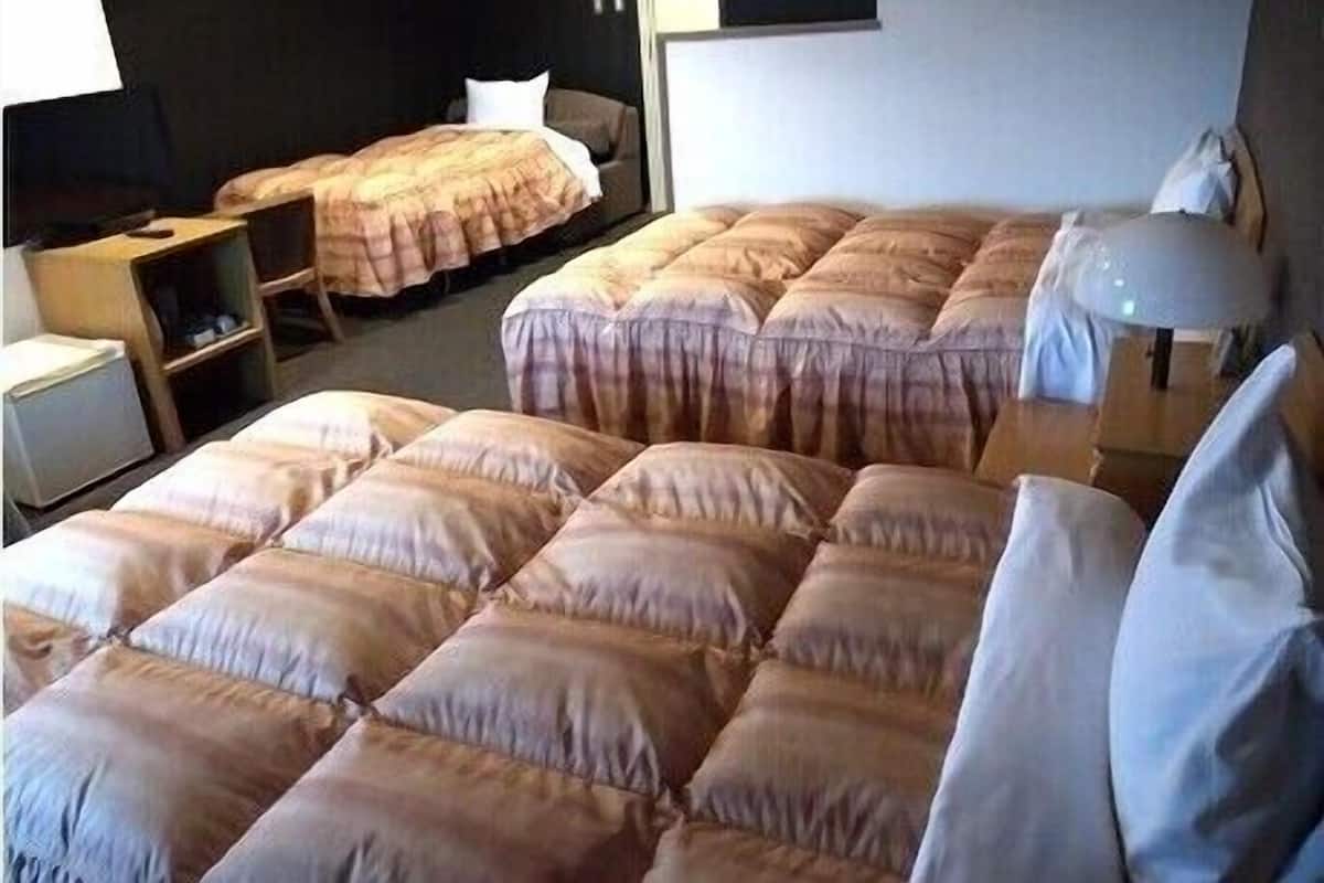 Habitació d'hotel amb diversos llits, una taula, una cadira i una làmpada.