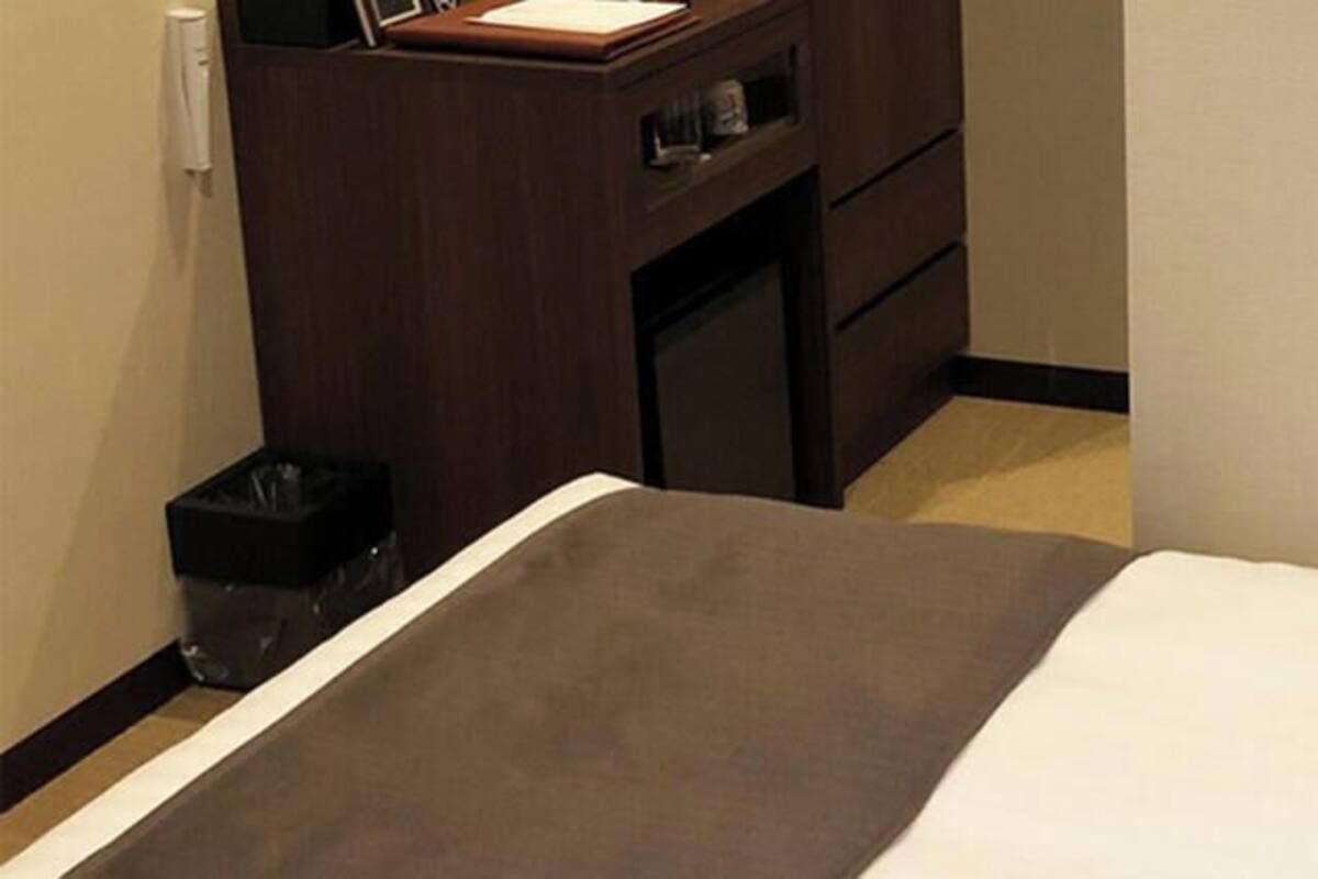 Une chambre d’hôtel avec un lit, une commode en bois et une poubelle.