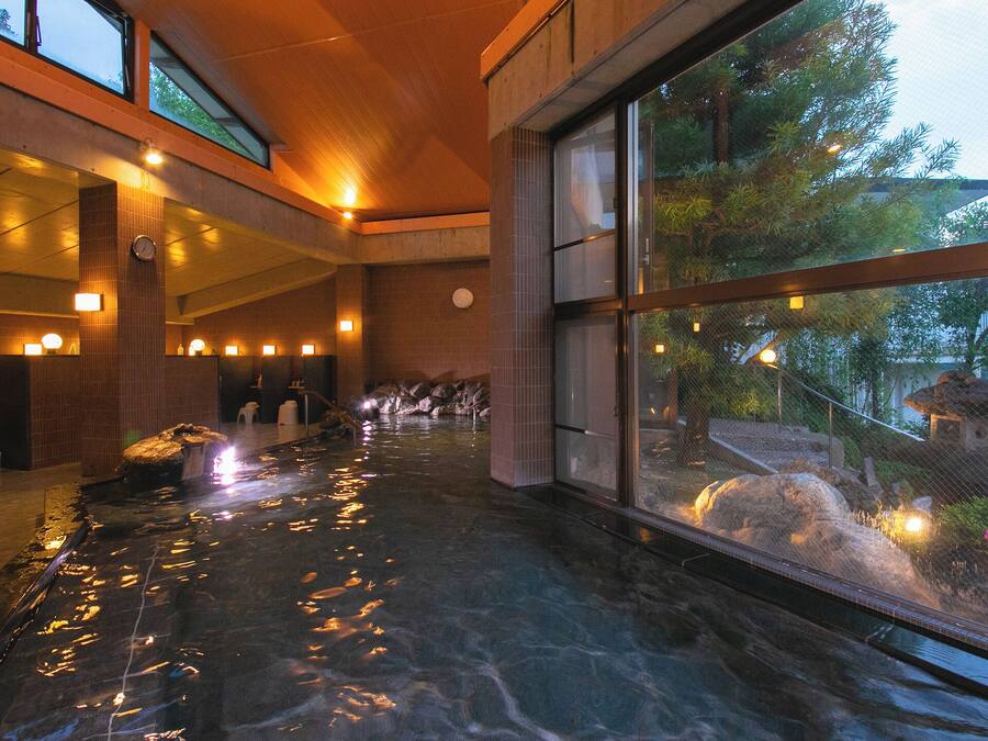 A hotel lobby with a reception desk, a wet floor indicating recent cleaning, and a view of a garden through large windows.