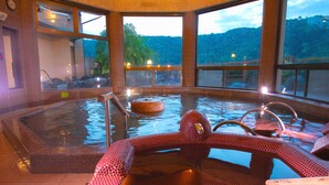 Un bain thermal avec une zone de sièges aux textures rouges, un banc en bois et une plateforme en pierre.