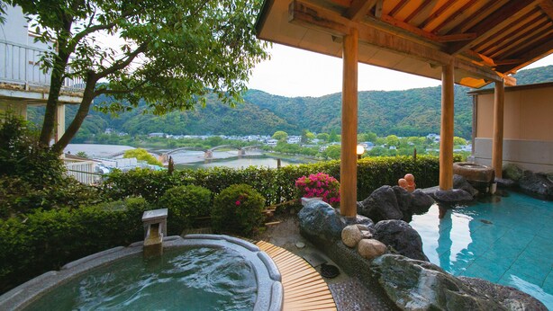 Un espace piscine intérieure paisible, avec vue sur une rivière et des montagnes, une terrasse en bois et des éléments décoratifs en pierre.