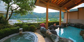 Un área de piscina interior tranquila con vistas a un río y montañas, terraza de madera y detalles de piedra.