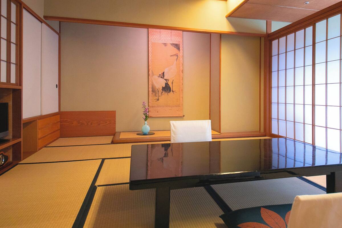 Une pièce de style japonais traditionnel, avec un sol recouvert de tatamis, une table basse, une chaise et des portes coulissantes.