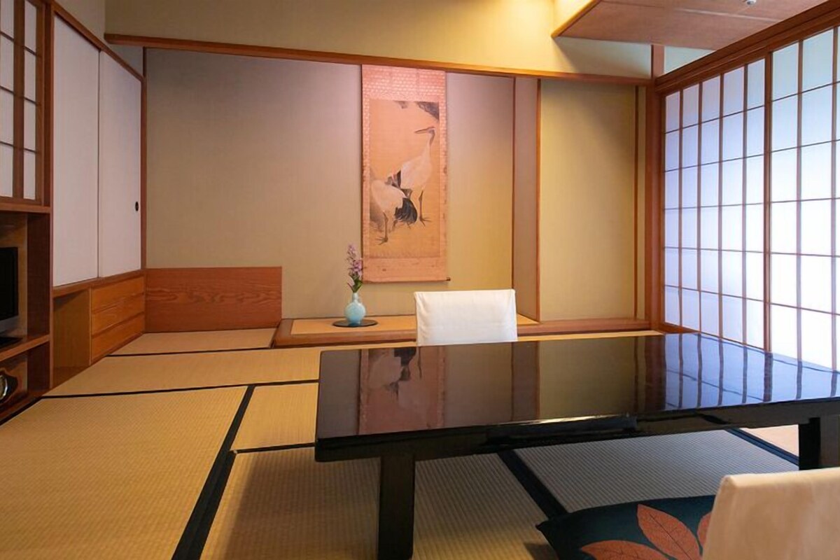 Ein traditioneller japanischer Raum mit Tatami-Böden, einem niedrigen Tisch, einem Stuhl und Schiebetüren.