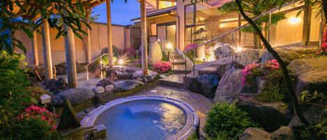 A serene outdoor pool area with a hot tub, surrounded by rocks and lush greenery.