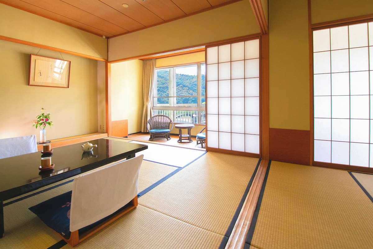 Une pièce de style japonais traditionnel, avec un sol recouvert de tatamis, une table basse, une chaise et une vue à travers un paravent shoji.