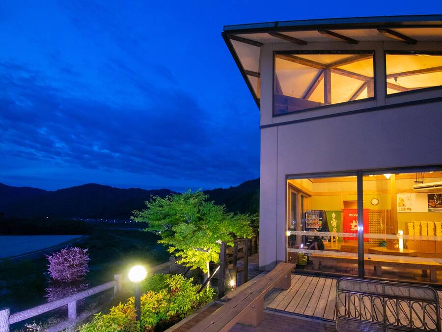 A modern building with a glass facade, a wooden deck, and a view of the surrounding landscape.