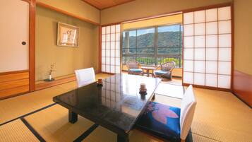 A traditional Japanese room with tatami flooring, a low table, and a view of a hillside.