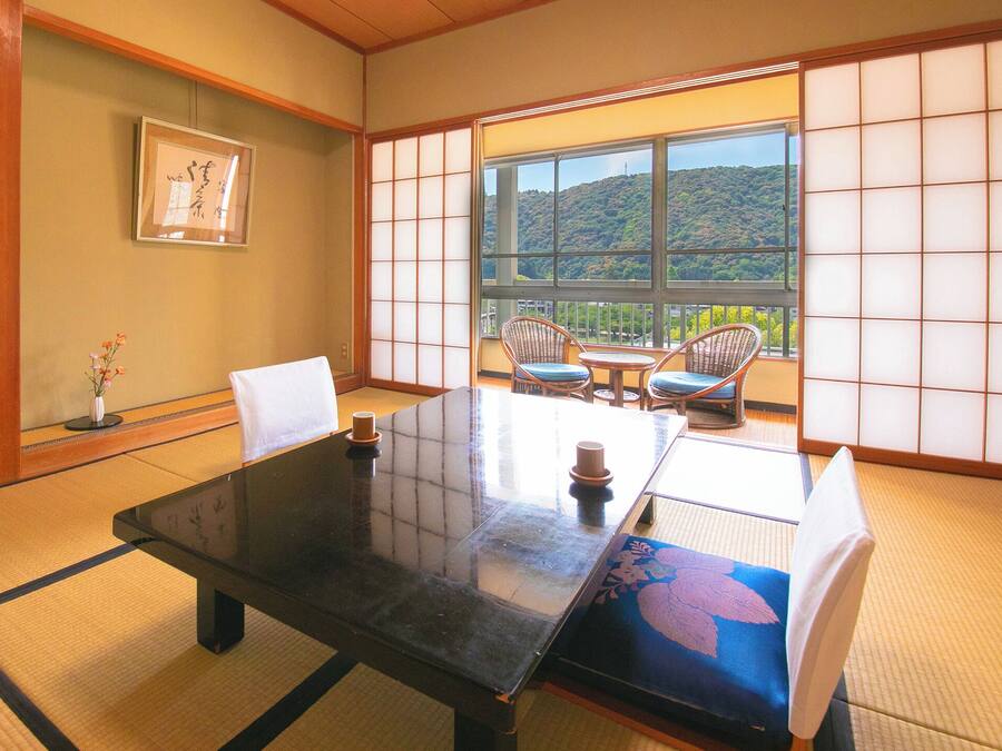 A traditional Japanese room with tatami flooring, a low table, and a view of a hillside.