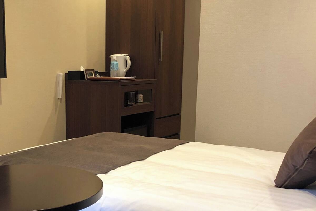 Une chambre à coucher comprenant un lit, une petite table, une armoire et un téléviseur fixé au mur.