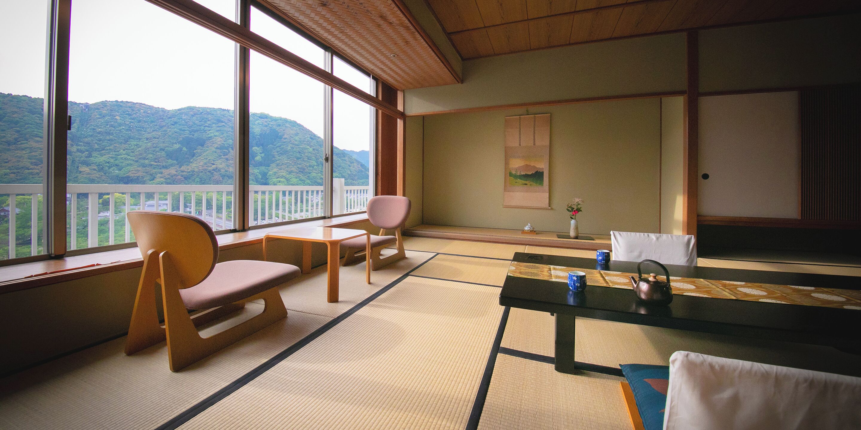 A traditional Japanese room with tatami flooring, a low table with a tea set, and a view of a mountain.