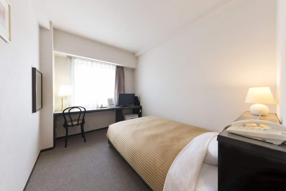 Une chambre d’hôtel équipée d’un lit, d’un bureau, d’une chaise et d’un téléphone posé sur une table de chevet.