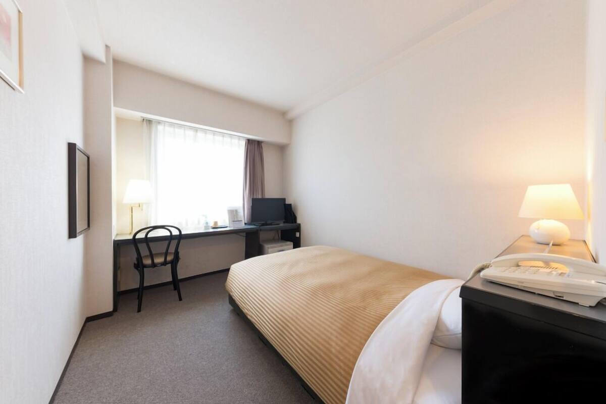 Une chambre d’hôtel équipée d’un lit, d’un bureau, d’une chaise et d’un téléphone.