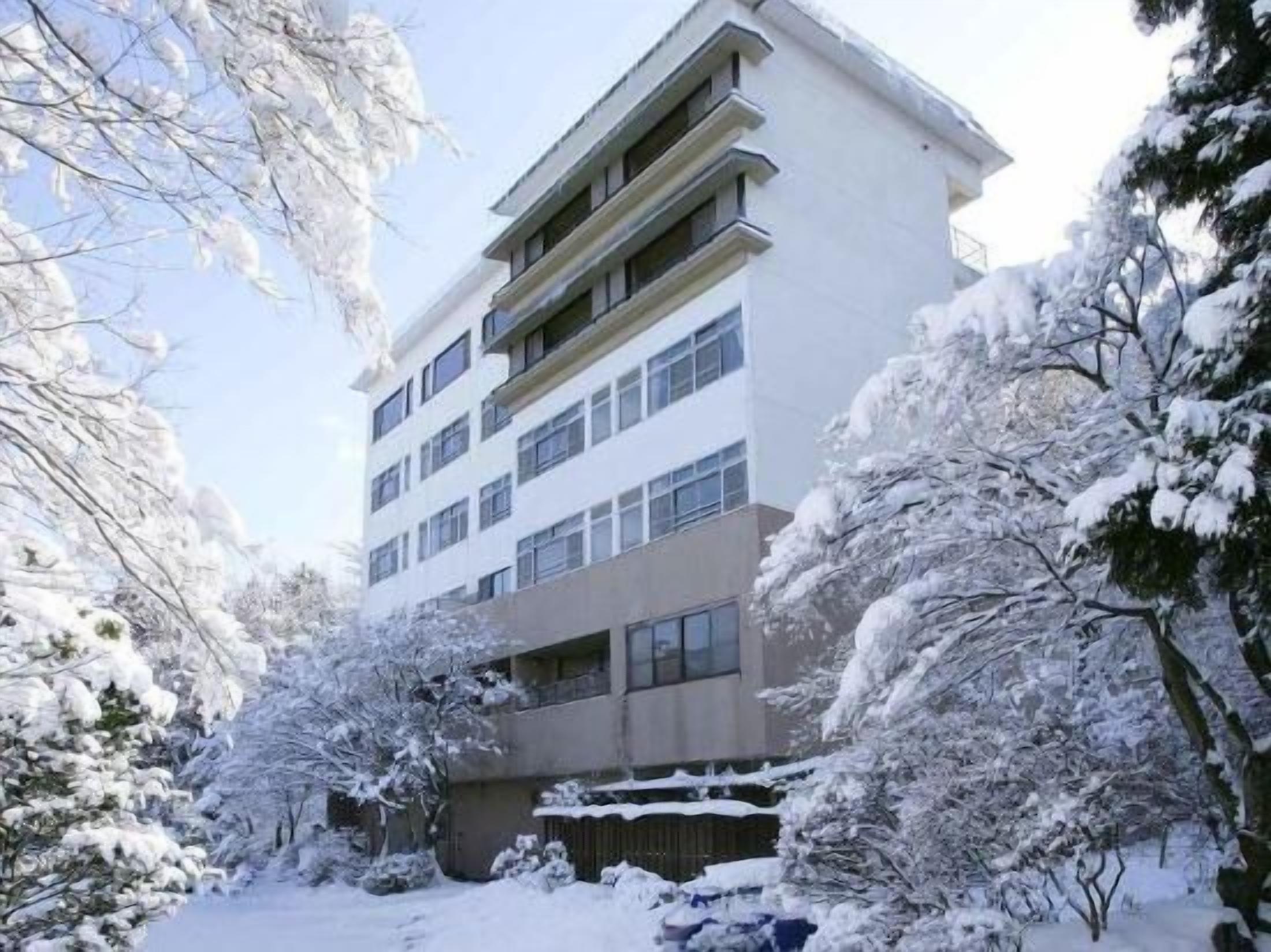 A multi-story building with a flat roof, surrounded by snow-covered trees.