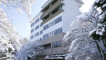 A multi-story building with a flat roof, surrounded by snow-covered trees.