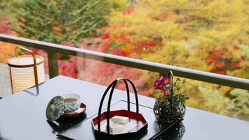 A table with a teapot, cup, and a red tray with a white object on a balcony with autumn foliage in the background.