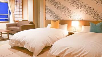 A hotel room with two beds, a sofa, a table, and a view of the outside.