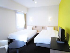Habitación de hotel con dos camas individuales, una mesita redonda pequeña, un escritorio con ordenador y una ventana con cortinas.