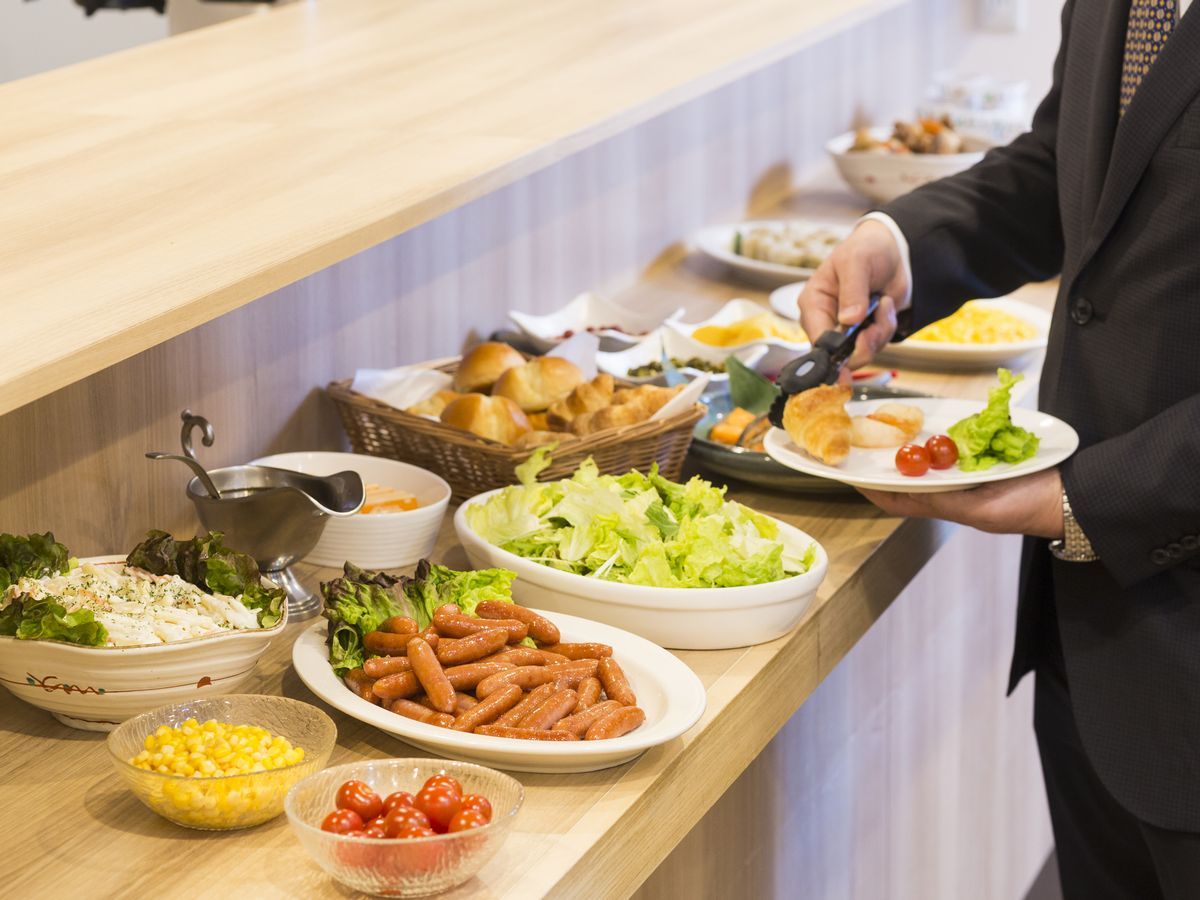 A buffet table with various food items and a person serving themselves.
