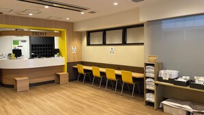 A hotel reception area with a reception desk, a waiting area with yellow chairs, and a counter displaying towels and amenities. - Smile Hotel - Utsunomiya Higashiguchi (Utsunomiya)