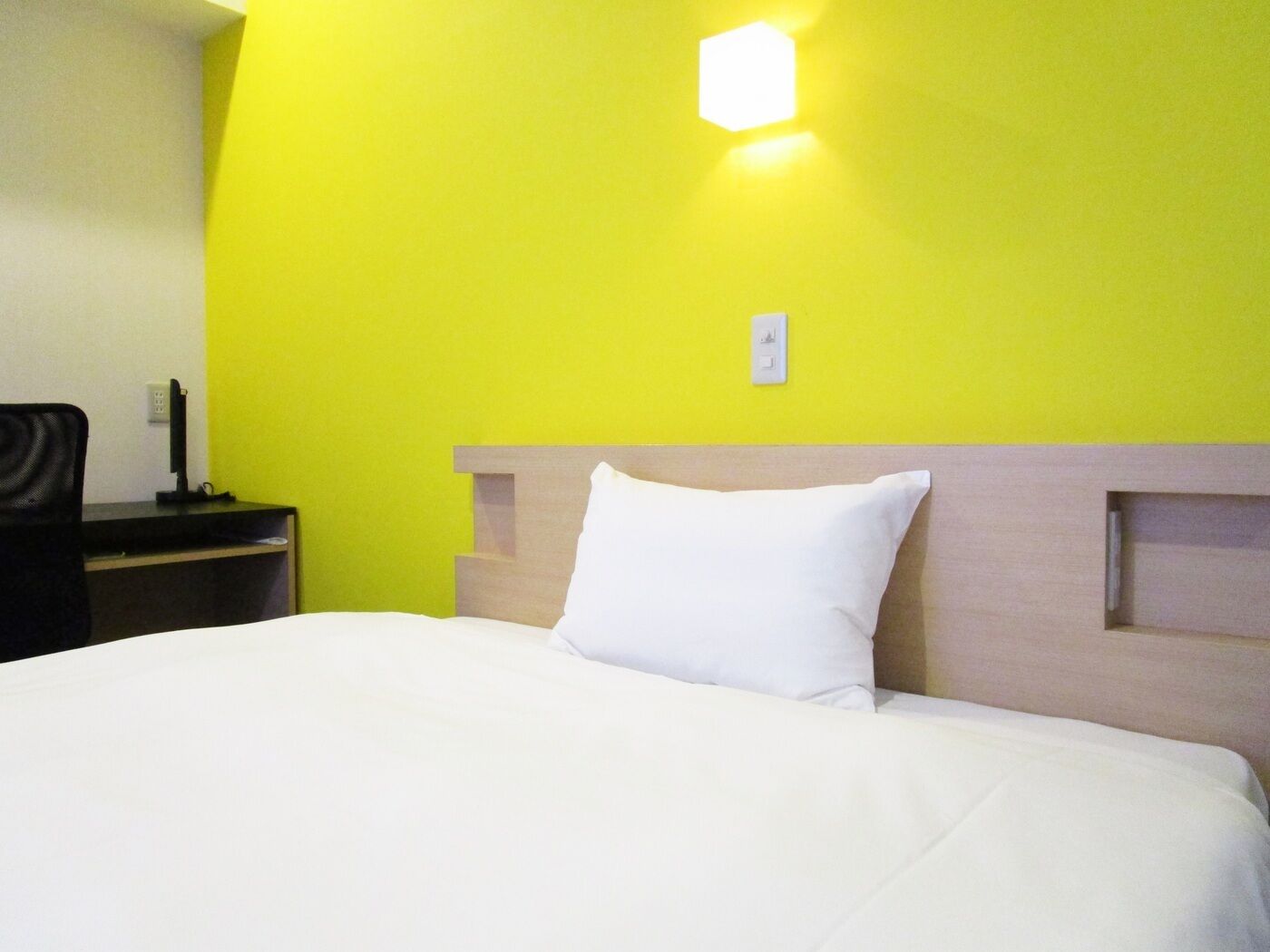Una camera d'albergo con un letto, un comodino, una lampada e una luce a parete.