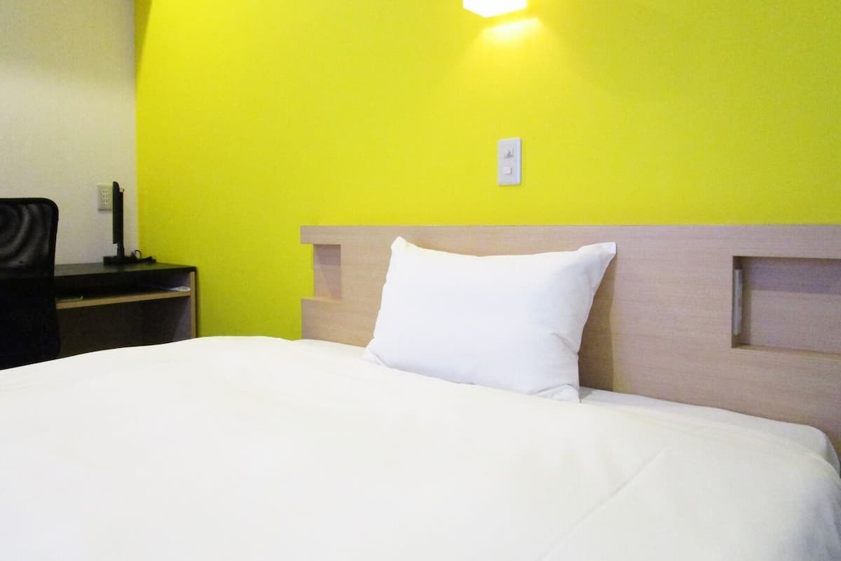 Quarto de hotel com uma cama, mesa de cabeceira, luminária e luz na parede.
