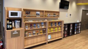 A hotel lobby with wooden shelving displaying books and magazines, a microwave, and a coffee machine. - Smile Hotel - Utsunomiya Higashiguchi (Utsunomiya)