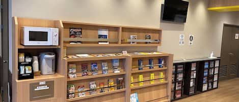 Un vestíbulo de hotel con estanterías de madera que exhiben libros y revistas, un microondas y una cafetera.