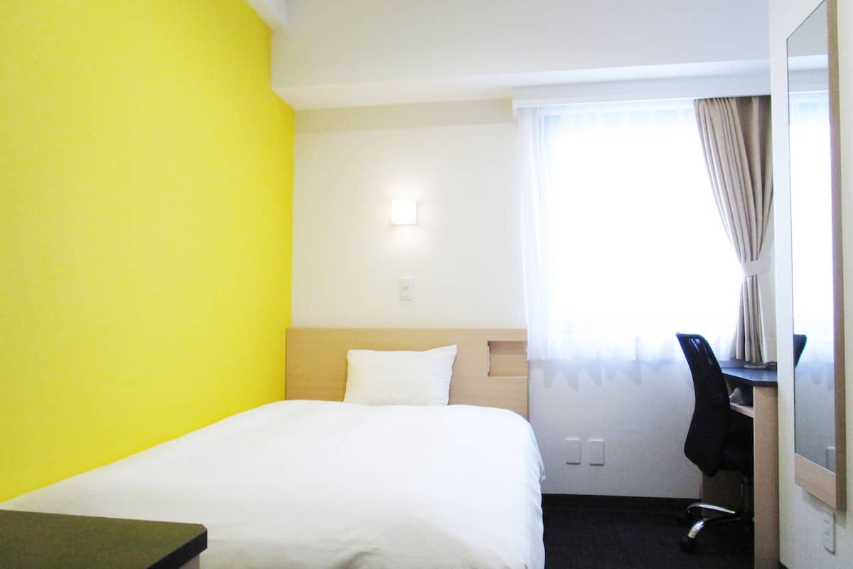 Quarto de hotel com uma cama, uma escrivaninha e uma cadeira.