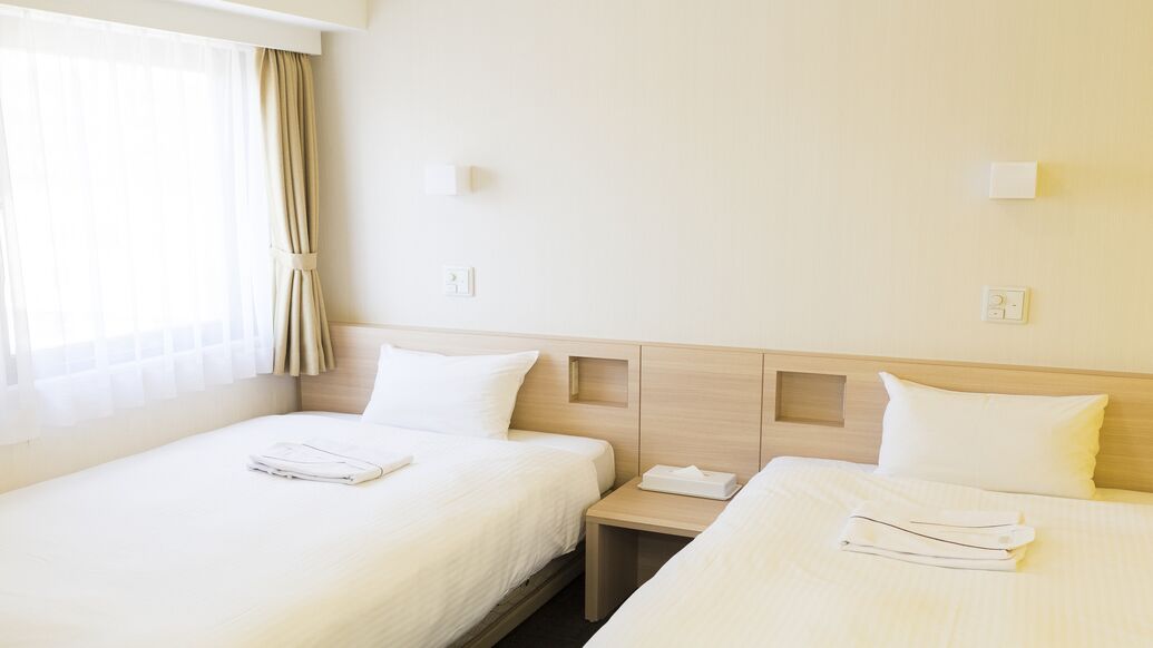 Una camera d'albergo con due letti, un comodino e una finestra con tende.