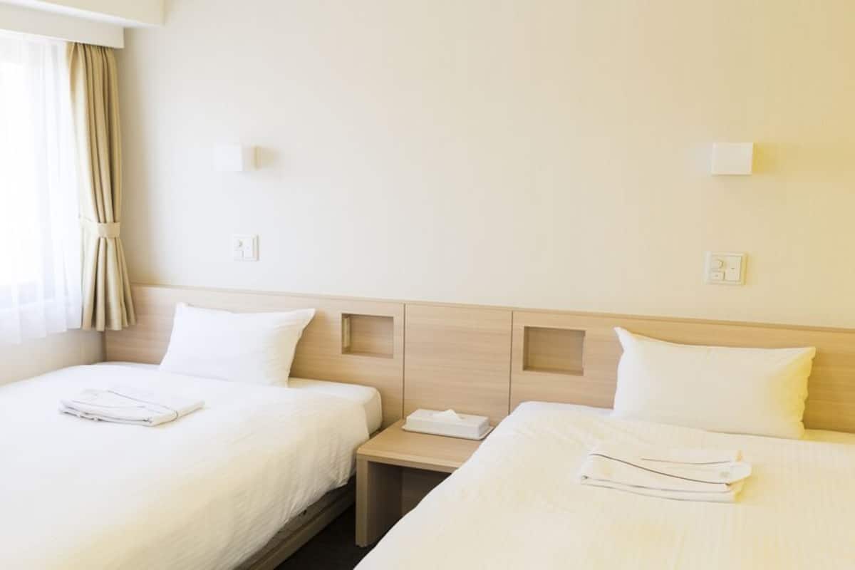 Quarto de hotel com duas camas, uma mesa de cabeceira e uma janela com cortinas.
