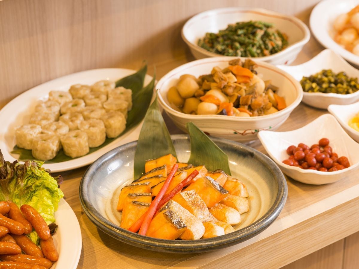 A variety of dishes on a table, including what appears to be a dish with sliced vegetables and possibly meat, a plate with dumplings, and other assorted food items.