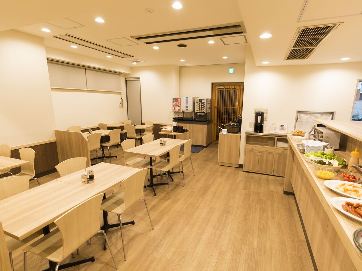 A modern dining area with multiple tables and chairs, a kitchen counter with food items, and a coffee machine.