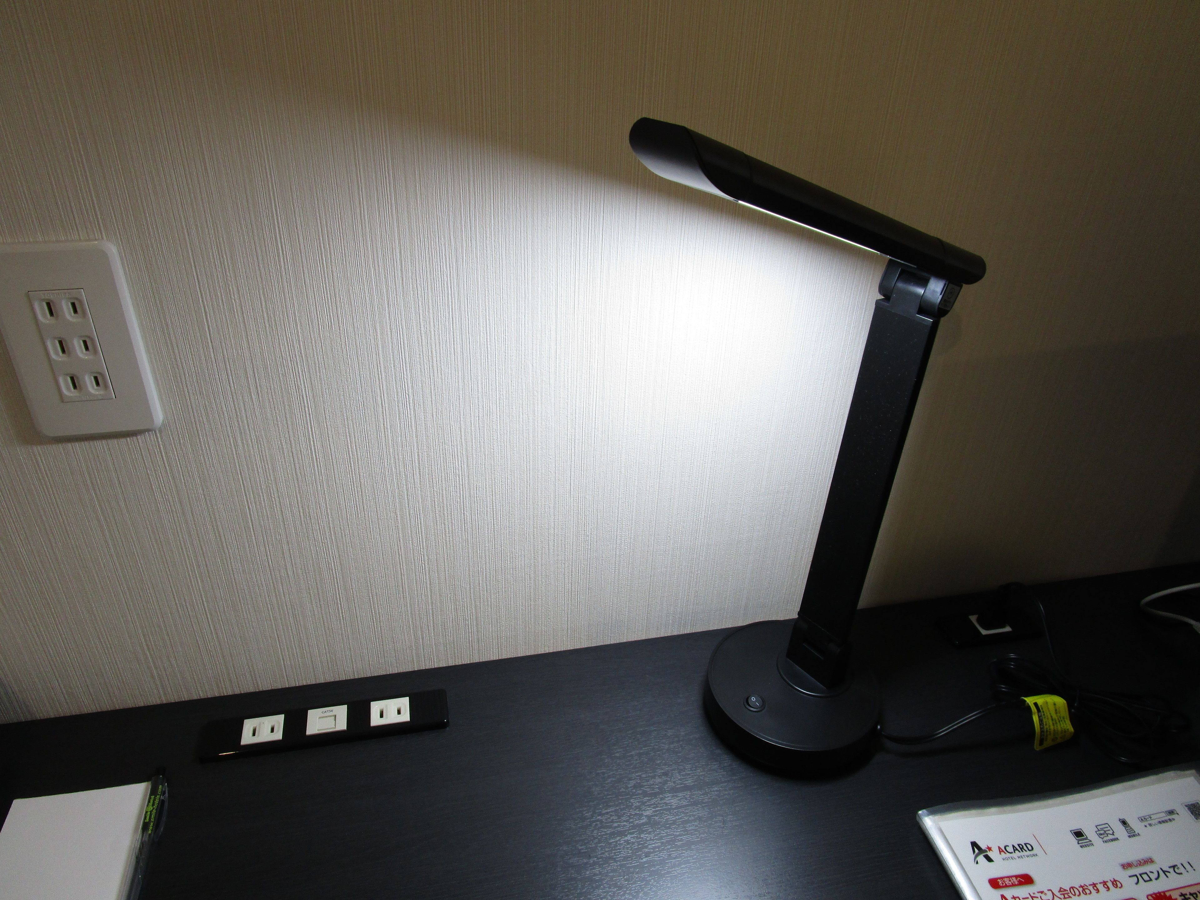 A desk with a black desk lamp, a power strip, and a white sign with Japanese text.
