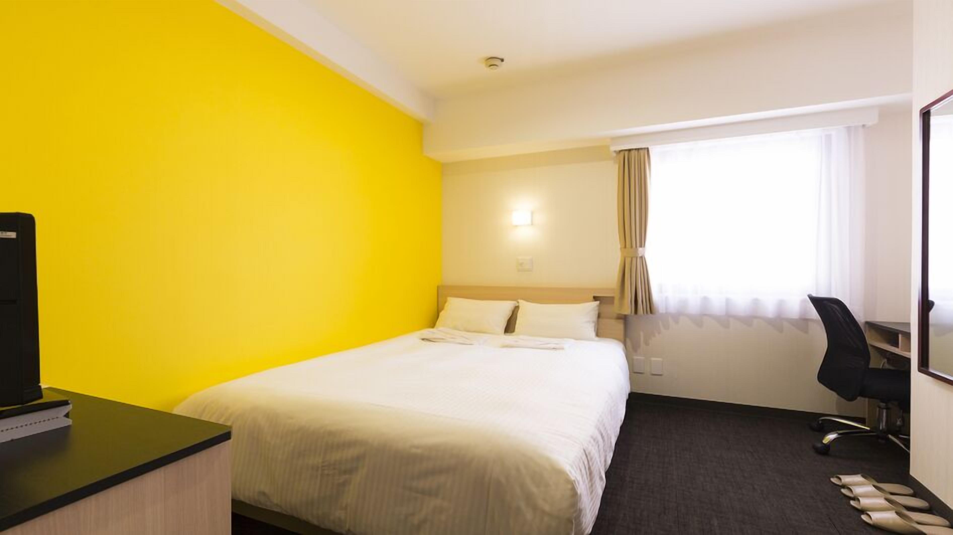 Una camera d'albergo con un letto, una scrivania, una sedia e una finestra con tende.