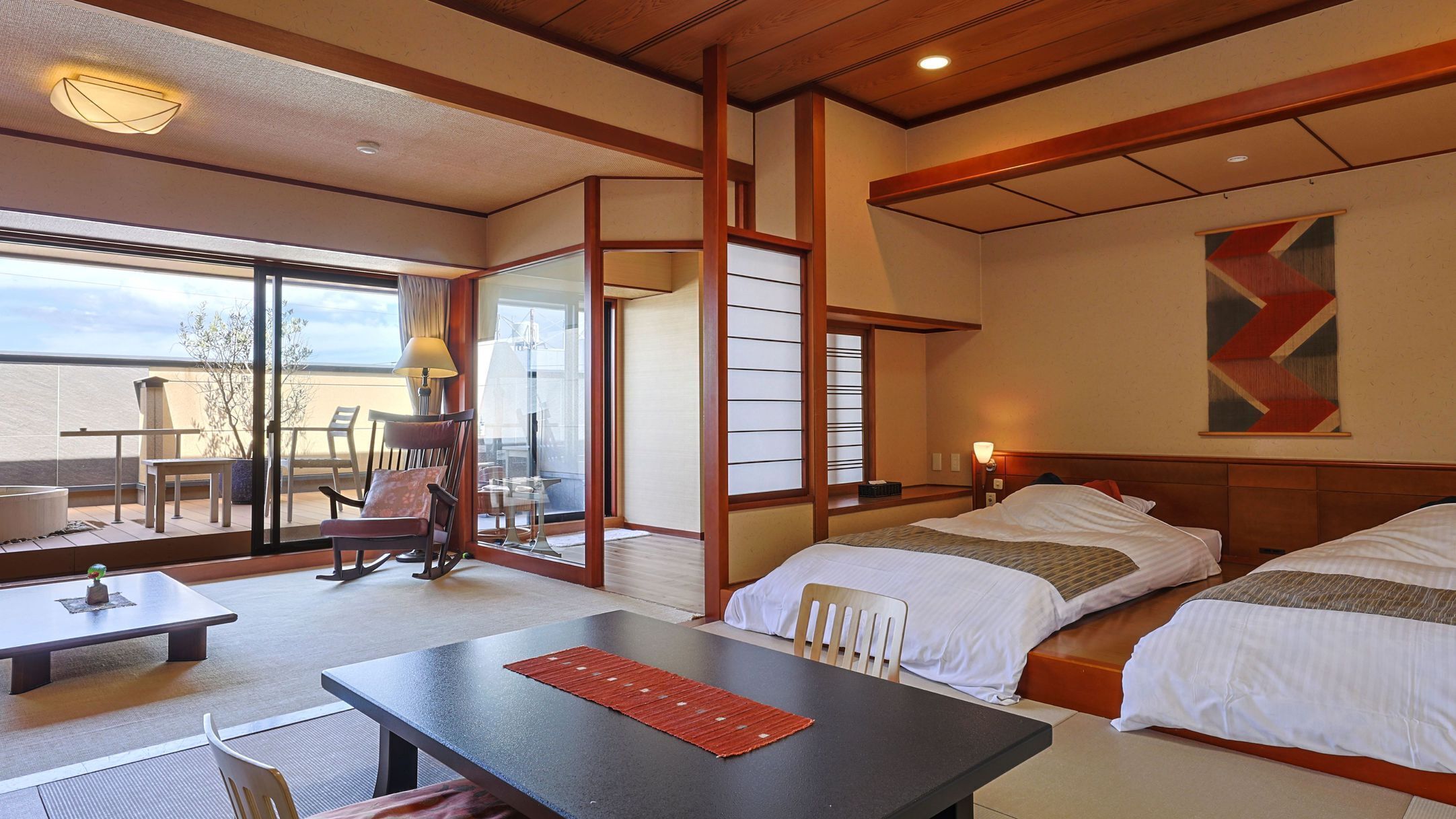 A hotel room with a balcony, a desk, two beds, and a large window.