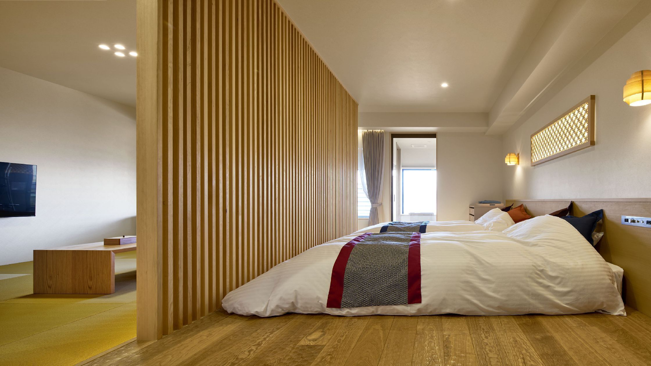 A hotel room with a large bed, a TV, a wooden partition, and a window.